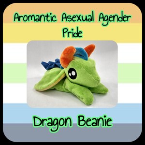 May include: A green plush dragon beanie with orange and blue accents. The beanie has large black eyes and is displayed against a background with the text "Aromantic Asexual Agender Pride" and "Dragon Beanie".