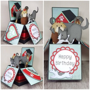 May include: A handmade pop-up birthday card featuring dog-themed cutouts. The card has a multi-layered design with a red and black base, light blue panels, and decorative elements like hearts, paw prints, and the words "Happy Birthday".