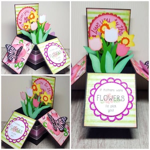 Può includere: Un biglietto pop-up fatto a mano con un tema floreale. Il biglietto presenta tulipani, narcisi e farfalle di carta. Il testo "If Mothers were FLOWERS I'd pick you!" è visualizzato sul biglietto. Il biglietto è decorato con accenti rosa, verdi e gialli.