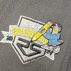 May include: A gray baseball cap with a silver and black embroidered patch featuring a cartoon character holding a yellow pencil. The patch says "BURDMAN 2023".