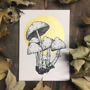 May include: A black and white illustration of a group of mushrooms with a gold background. The mushrooms are drawn in a detailed style with a focus on their caps and stems.