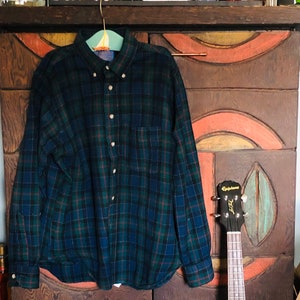 May include: A blue and green plaid flannel shirt hanging on a hanger in front of a wooden cabinet with a red, orange, and yellow painted design. A red, yellow, and orange ukulele is leaning against the cabinet.