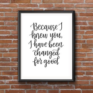 以下が含まれることがあります： 黒いフレームに入ったプリントで、白い背景に「Because I knew you, I have been changed for good」という引用句がエレガントな筆記体で書かれています。レンガの壁に飾られています。