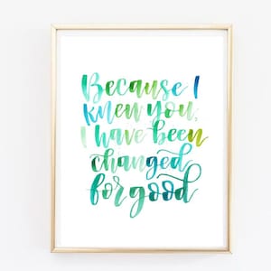 May include: A framed art print featuring the quote "Because I knew you, I have been changed for good" in watercolour lettering. The text is in shades of green and blue on a white background, framed in light wood.