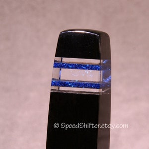May include: A black, rectangular object with two horizontal bands of blue glitter encased in clear resin. The top of the object is rounded. The Etsy shop name "SpeedShifter.etsy.com" is printed at the bottom.