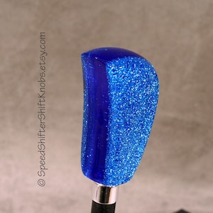 Puede incluir: Pomo de cambio azul brillante con acabado brillante. El pomo tiene una parte superior redondeada y una base plateada. El texto "SpeedShifterKnobs.etsy.com" es visible en el lado izquierdo de la imagen.