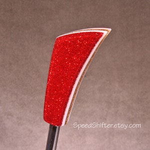 May include: A red glitter-covered gear shift knob with white and gold accents. The curved design features a shiny, textured surface. The base is a silver metal rod. The Etsy shop name SpeedShifter.etsy.com is visible.