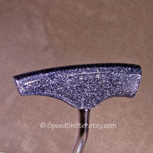 Op de afbeelding: Een aangepaste auto versnellingspookknop met een glinsterende, donkerzilveren afwerking. De knop heeft een gebogen, ergonomisch ontwerp en is gemonteerd op een gepolijste metalen steel. De Etsy shopnaam, SpeedShifter.etsy.com, is op de afbeelding gedrukt.