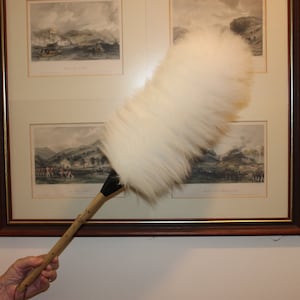 Peut inclure: Un plumeau blanc avec un long manche en bois. Le plumeau est utilisé pour nettoyer un tableau encadré représentant une scène de paysage.