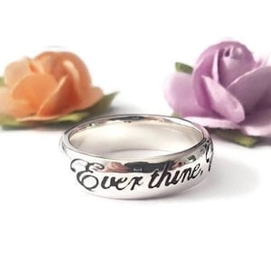 May include: A silver ring with the inscription "Ever thine, " on the band. The ring is surrounded by two small artificial flowers, one orange and one purple.