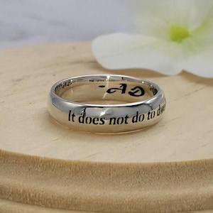 May include: A silver band ring with the inscription "It does not do to dwell on dreams and forget to live" engraved on the outside.