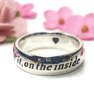 May include: A silver ring with the inscription "Love it, on the inside" engraved on the band. The ring has a small heart shape cut out on the top.