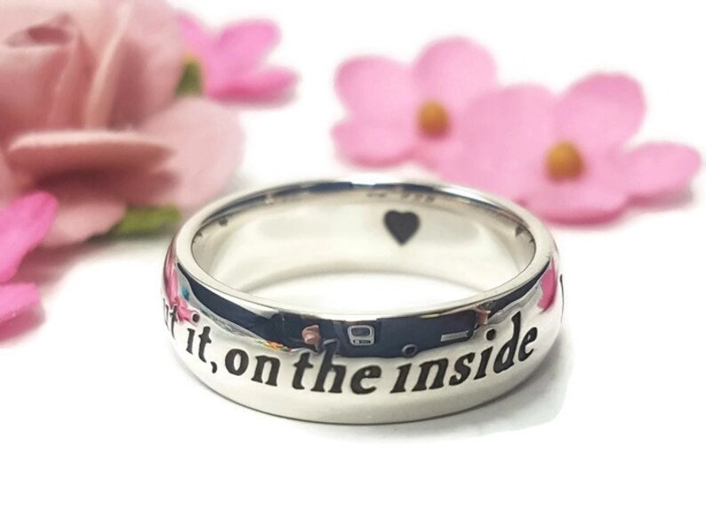 May include: A silver ring with the inscription "Love it, on the inside" engraved on the band. The ring has a small heart shape cut out on the top.