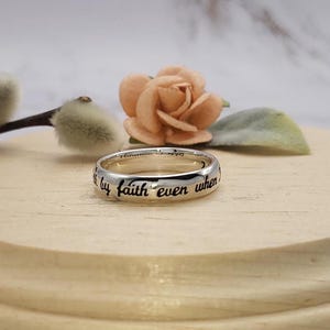 Puede incluir: Un anillo de banda de plata con la inscripci&oacute;n "Camino por fe incluso cuando no puedo ver" grabada alrededor de la banda.