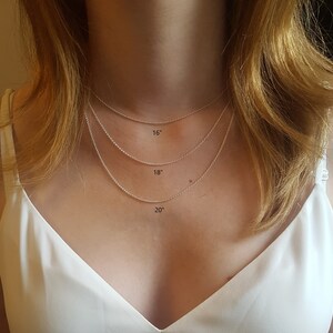 May include: Three silver chains of different lengths, 16 inches, 18 inches, and 20 inches, are shown on a person's neck. The chains are delicate and have a subtle shine.
