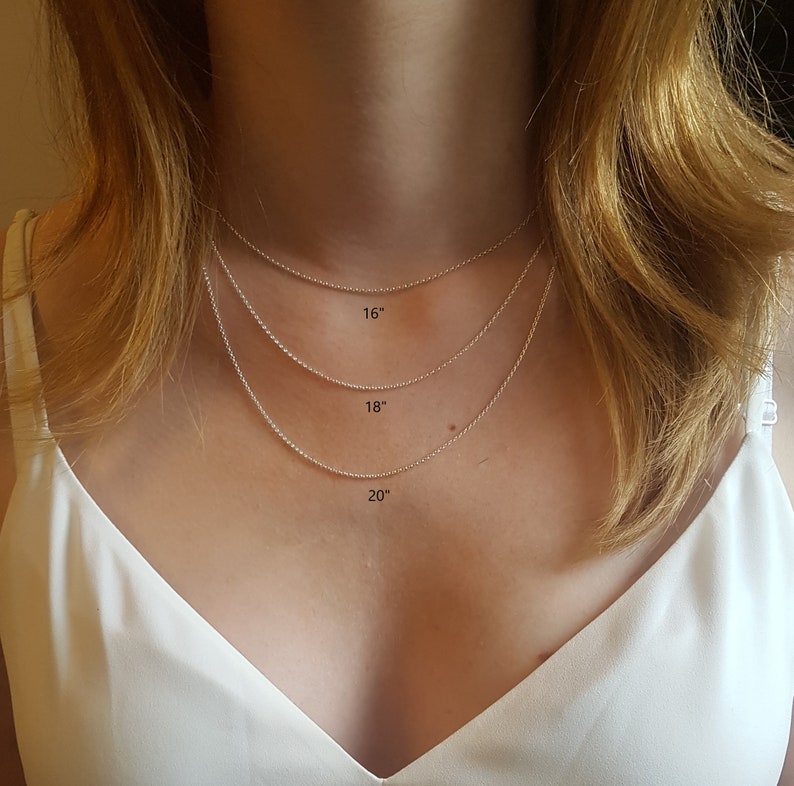 May include: Three silver chains of different lengths, 16 inches, 18 inches, and 20 inches, are shown on a person's neck. The chains are delicate and have a subtle shine.