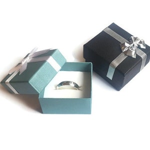 May include: Two small gift boxes, one black and one teal, with silver ribbon and bows. The teal box is open and contains a silver ring.