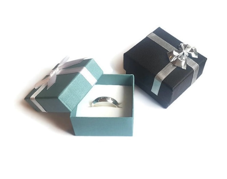 May include: Two small gift boxes, one black and one teal, with silver ribbon and bows. The teal box is open and contains a silver ring.