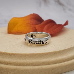 May include: A silver ring with the words "Paratus" and an umbrella symbol engraved on it.