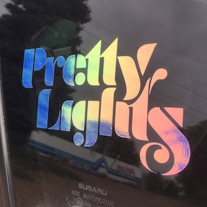 May include: A rainbow-colored vinyl sticker with the text "Pretty Lights" in a stylized font.