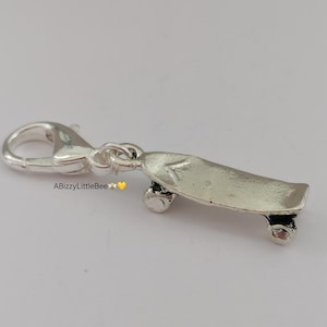 May include: Silver charm in the shape of a skateboard with a silver clasp. The skateboard has black wheels.