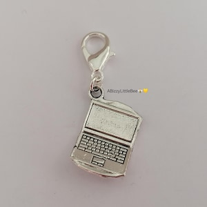 May include: Silver charm in the shape of a laptop computer. The charm has a silver loop for attaching to a zipper or bag.