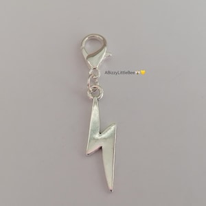 May include: Silver charm featuring a lightning bolt design. The charm has a lobster clasp for attaching to a bracelet or necklace.