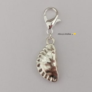 May include: Silver charm shaped like a half-eaten pastry with a textured crust. The charm is attached to a silver lobster clasp.