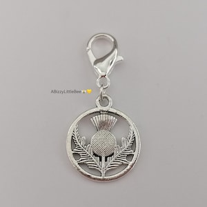 May include: Silver charm featuring a detailed design of a thistle flower. The charm is attached to a silver split ring.