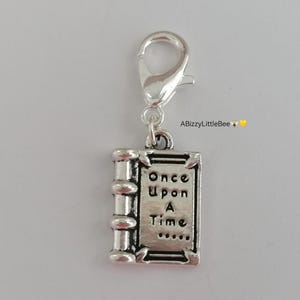 May include: Silver charm shaped like a book with the words "Once Upon A Time..." on the cover. The charm is attached to a silver lobster clasp.