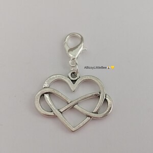May include: Silver charm featuring an infinity symbol intertwined with a heart shape. The charm has a lobster clasp for attaching to a bracelet or necklace.