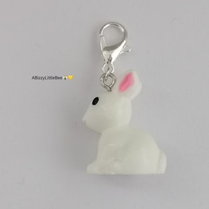 Peut inclure: Un charme de lapin blanc avec des oreilles roses et des yeux noirs attaché à un fermoir à homard argenté.