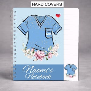 May include: A spiral-bound notebook with a light blue cover featuring a stylized illustration of a medical scrub top. The design includes a red heart, floral accents, and the text "Naomi's Notebook". The top of the notebook reads "HARD COVERS".