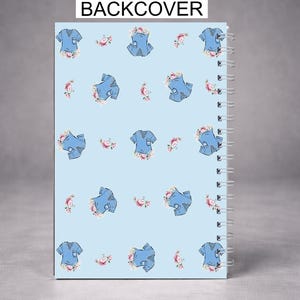 May include: A spiral-bound notebook with a light blue cover featuring a pattern of blue scrubs and pink floral accents. The text "BACKCOVER" is printed at the top. The notebook is designed for note-taking and journaling.
