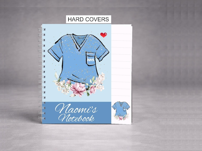May include: A spiral-bound notebook with a light blue cover featuring a medical scrubs design, a red heart, and the text "Naomi's Notebook." The cover also includes floral accents and the text "HARD COVERS."