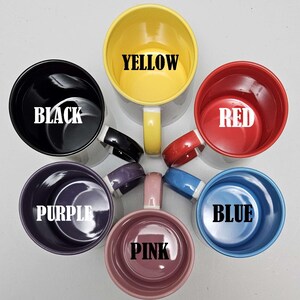 May include: Six ceramic mugs in different colors, including black, yellow, red, purple, pink, and blue. Each mug has the color name written in white letters on the inside.