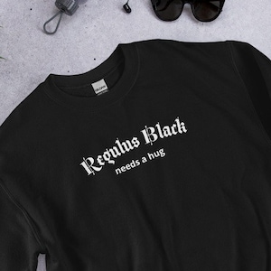 以下が含まれることがあります： 「Regulus Black needs a hug」という白い文字が書かれた黒いスウェットシャツ。