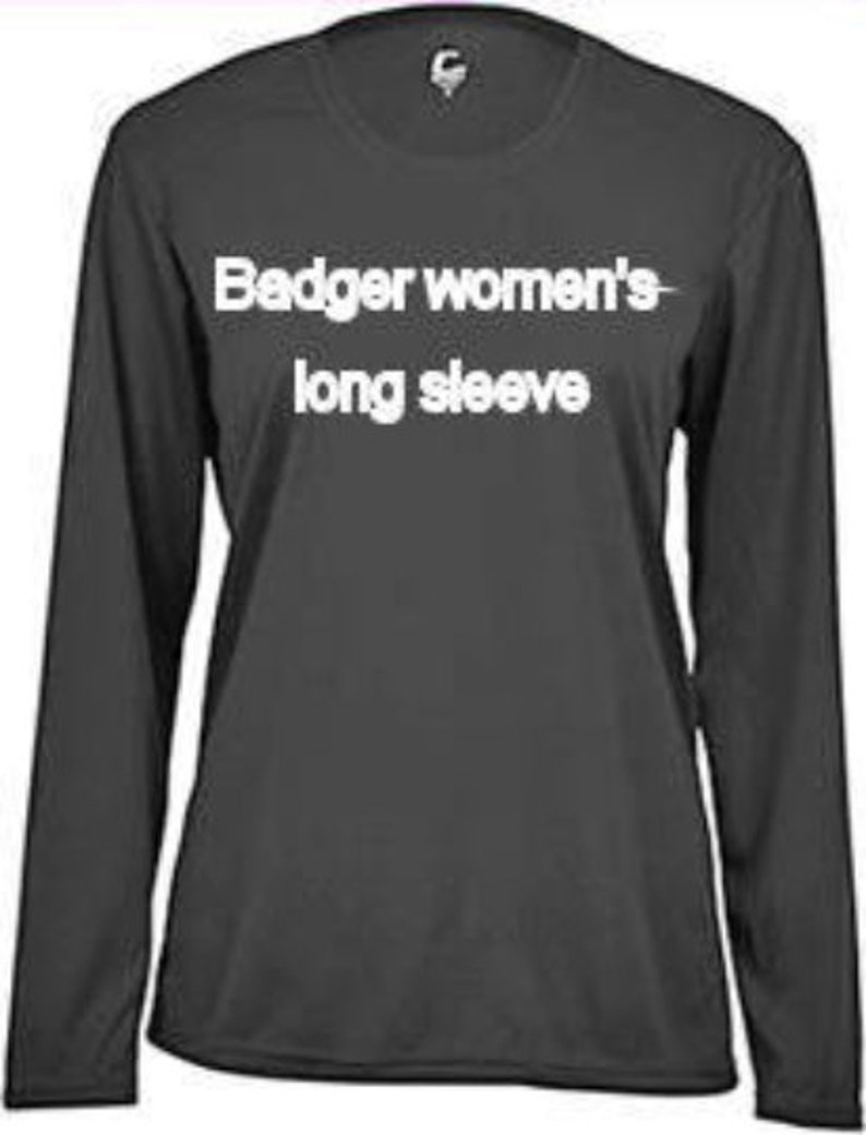 May include: A dark gray long-sleeve shirt with the text "Badger women's long sleeve" in white. The shirt has a crew neck and a small logo near the neckline. The fabric appears to be a lightweight material.