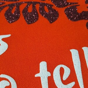 May include: Orange fabric with white glitter text that reads "She's telling" and a black glitter floral design.