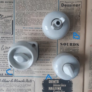 Peut inclure: Trois interrupteurs en céramique blanche de forme rectangulaire arrondie. Les interrupteurs ont un petit bouton triangulaire en relief au centre. Les interrupteurs sont disposés en forme de triangle sur une page avec du texte en français.