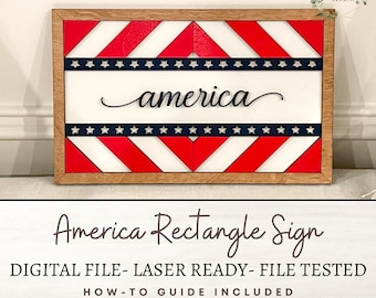 May include: A laser-cut wooden sign with a red, white, and blue chevron pattern and the word "america" in a cursive font. The sign is framed in a natural wood frame.