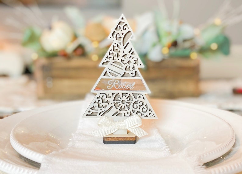 Puede incluir: Porta tarjetas de lugar de &aacute;rbol de Navidad de madera blanca con un lazo blanco y el nombre "Robert" escrito en &eacute;l.