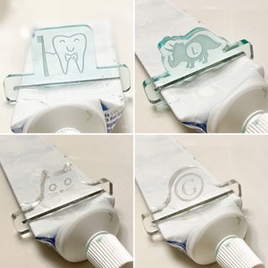 May include: Four clear plastic toothpaste squeezers with different designs. The designs include a tooth with a toothbrush, a dinosaur, a cat, and a letter G. Each squeezer is attached to a tube of toothpaste.