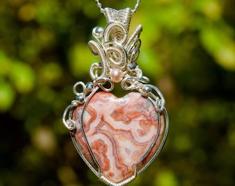 May include: A silver wire wrapped heart pendant with a pink and white agate stone. The pendant features a delicate silver wire design with a small pearl accent.