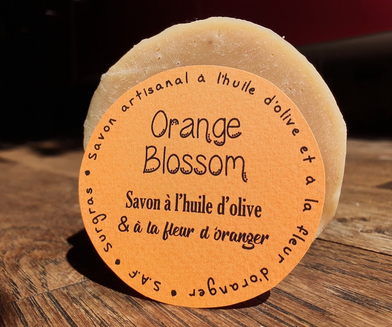 May include: A round bar of orange blossom soap with a label that reads "Savon artisanal a l'huile d'olive et a la fleur d'oranger S.A.F. Orange Blossom Savon &agrave; l'huile d'olive & &agrave; la fleur d'oranger"