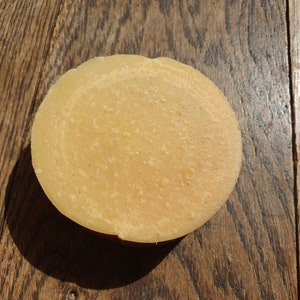 May include: A round, pale yellow bar of soap with a swirl pattern on a wooden surface.