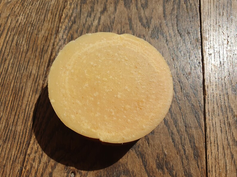 May include: A round, pale yellow bar of soap with a swirl pattern on a wooden surface.