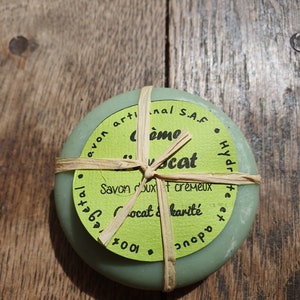 May include: A green round bar of soap wrapped in twine. The label reads "Savon doux et cremeux" and "Cococat & karit&eacute;".