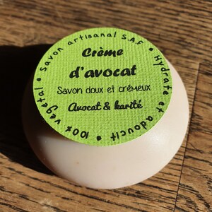 May include: A green and white round soap bar with the text "Savon artisanal S.A.F. Cr&egrave;me d'avocat Hydrate Savon doux et cr&eacute;meux Avocat & karit&eacute; 100%"