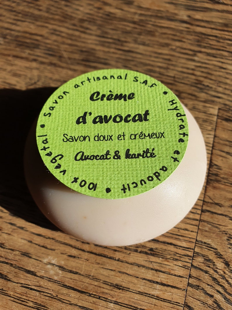 May include: A green and white round soap bar with the text "Savon artisanal S.A.F. Cr&egrave;me d'avocat Hydrate Savon doux et cr&eacute;meux Avocat & karit&eacute; 100%"